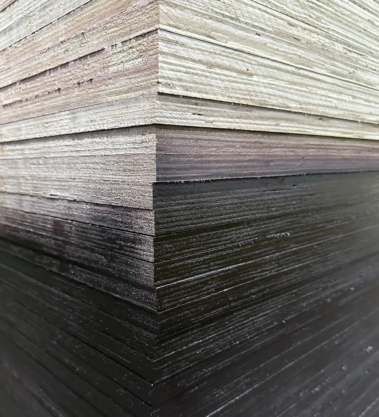 Corner of a tall film-faced plywood stack with pale layered core edges above and dark film-faced sheets below