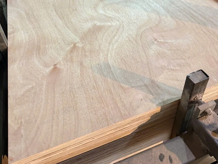 Okoume-faced plywood sheet with swirl figure on a stack held by a steel clamp post, layered edge in front